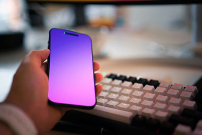 Hand holding a cellphone with a keyboard in the background.