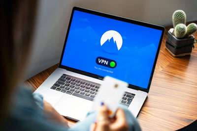 A person holding a credit card in front of a laptop with the screen displaying a “VPN” splash screen.